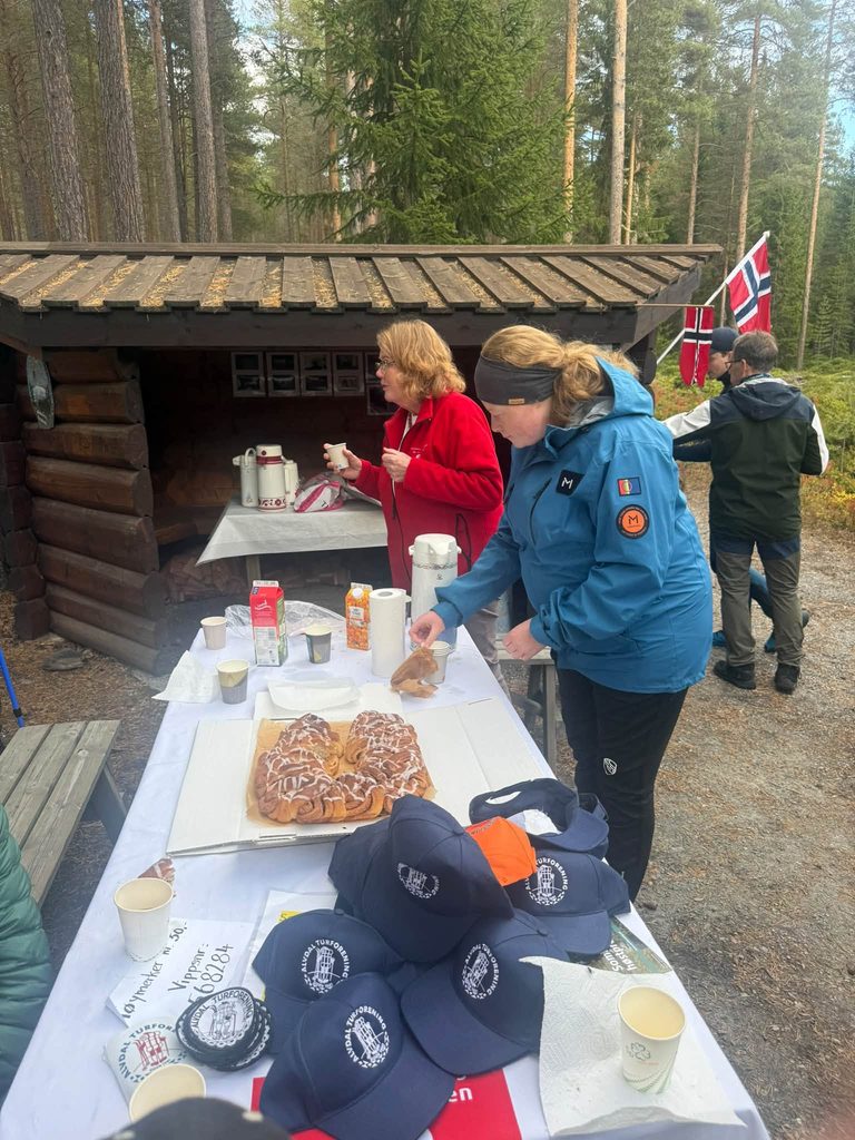 To kvinner ordner kaffe, saft og kanelsnurrer på et bord med caps fra Alvdal Turforening under arrangementet.